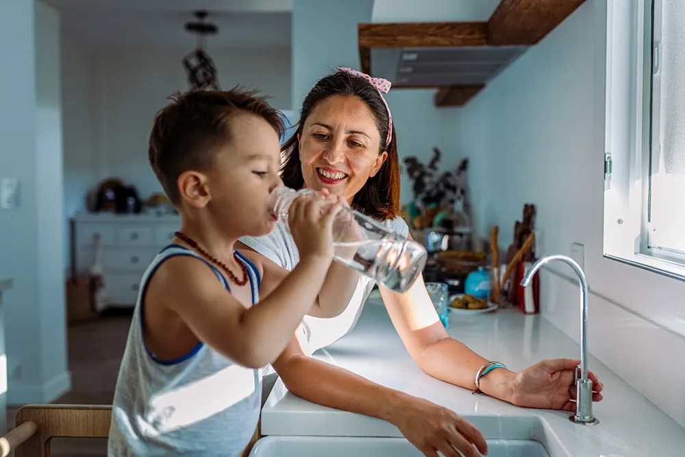 Photo of mother and son drinking water from a kitchen faucet